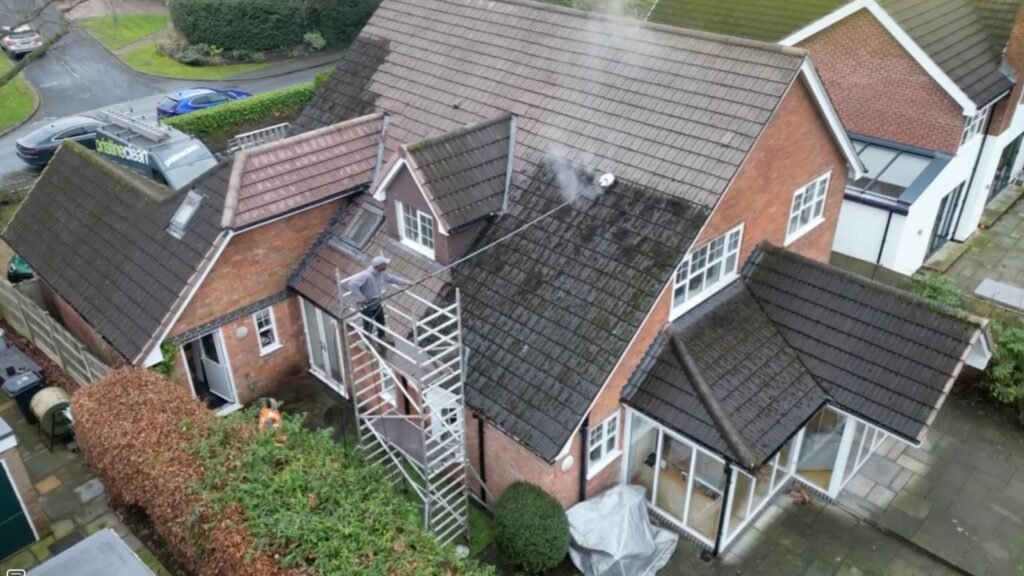 A professional roof clean is removing moss from a house in Altrincham. The use of professional tools including soft washing and the use of safety equipment shows a great job is being done.